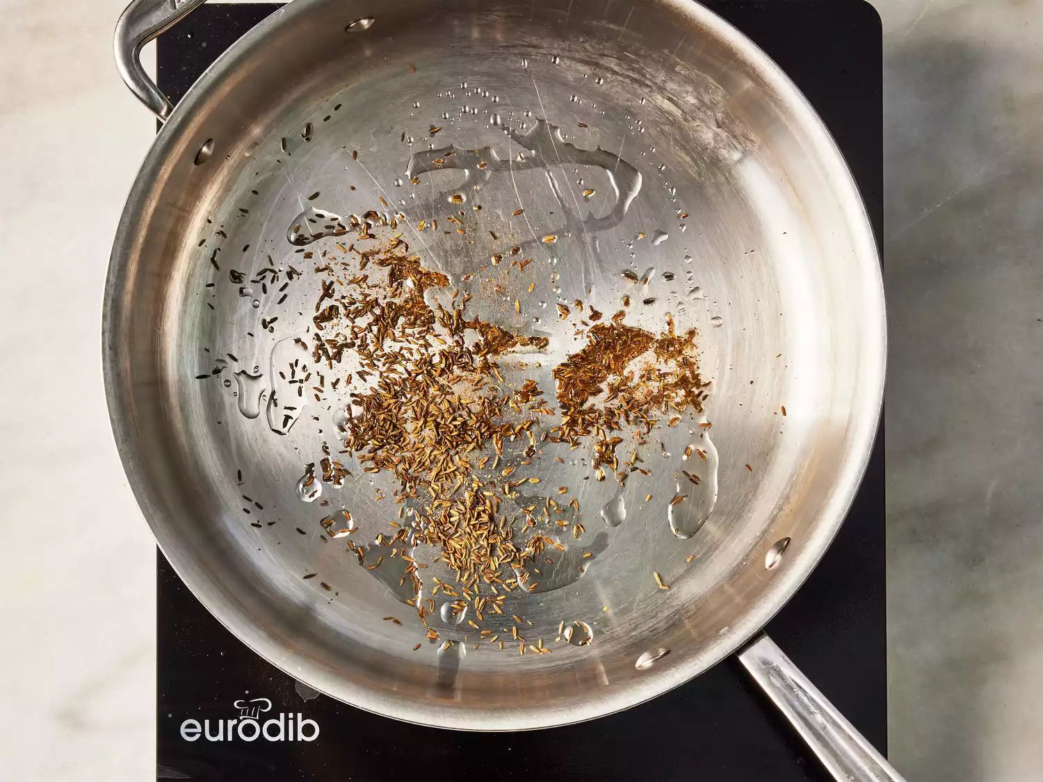 A large pan with cumin seeds frying in oil