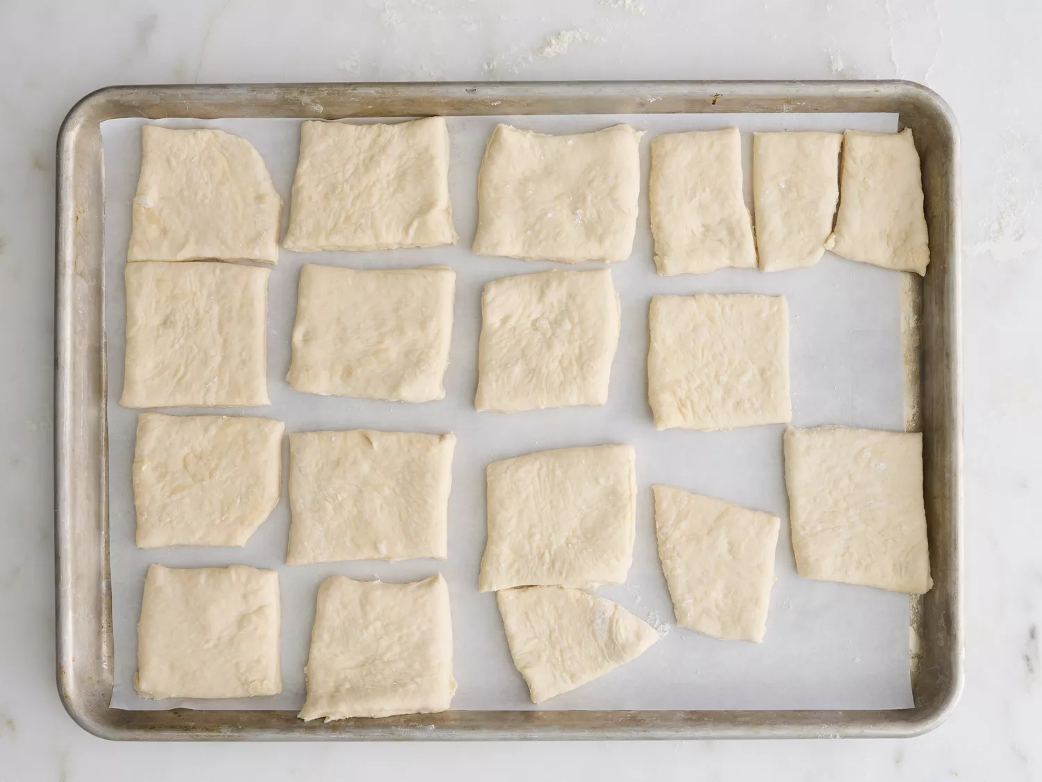 A parchment paper-lined baking sheet with squares of sopapilla dough