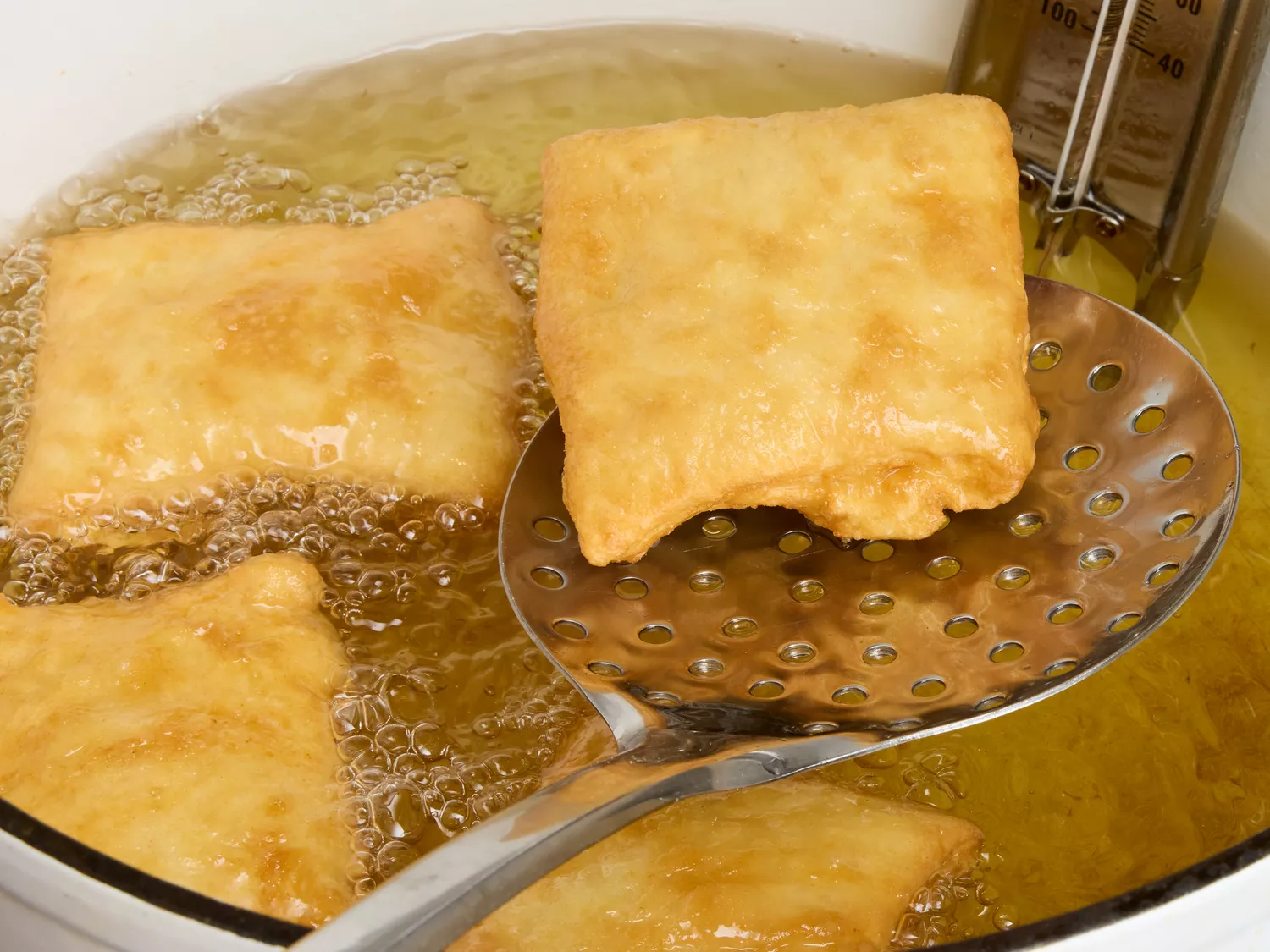 A golden brown fried sopapilla being lifted out of a pot of hot oil