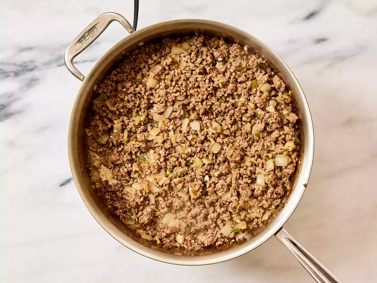 A large pan with browned, seasoned ground beef and chopped onion