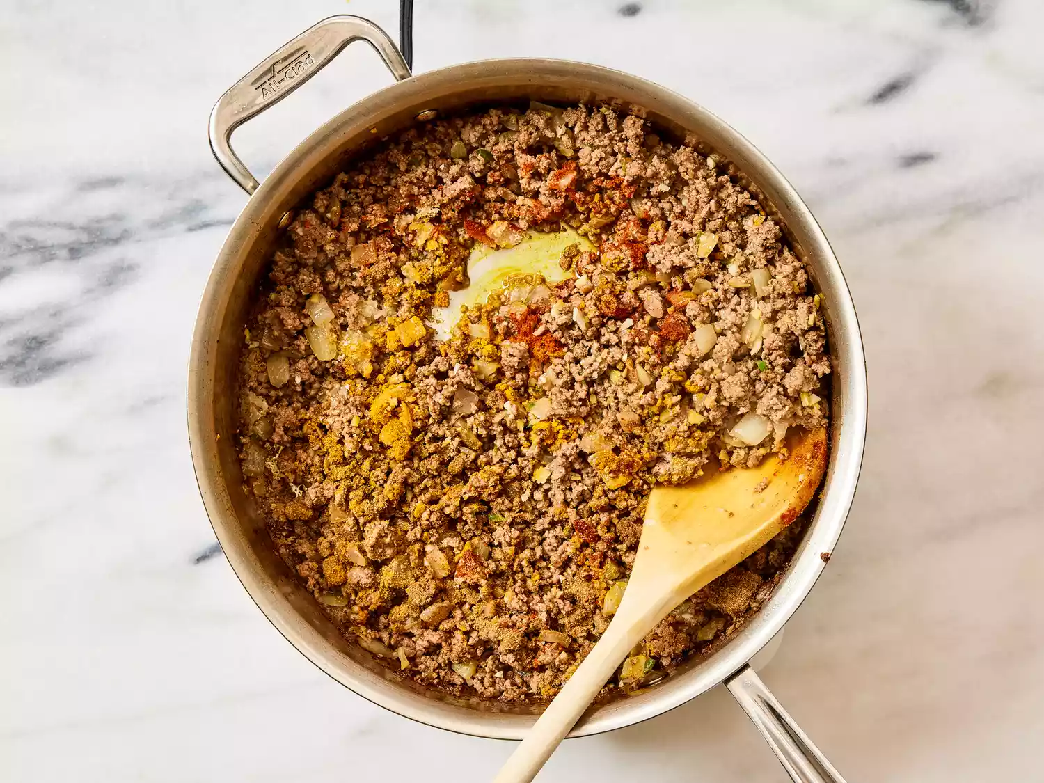 A pan of seasoned ground beef and onions being stirred with a wooden spoon