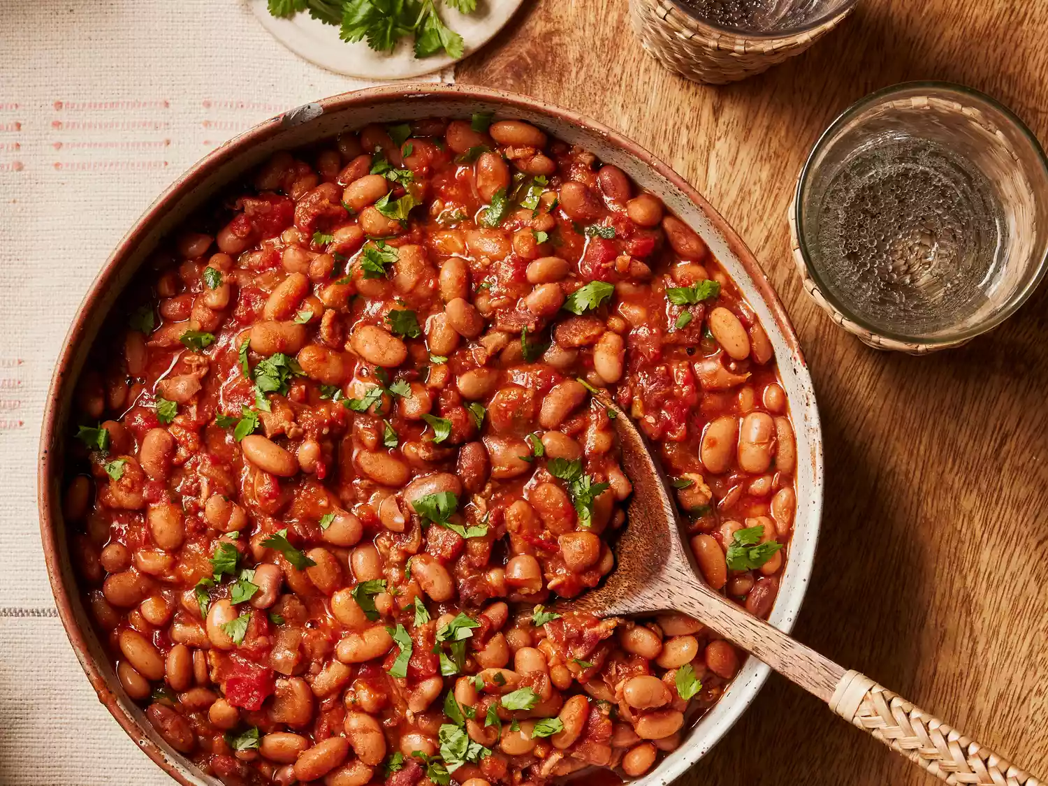 A serving bowl of pinto beans with Mexican-style seasoning topped with chopped cilantro with a large wood serving spoon