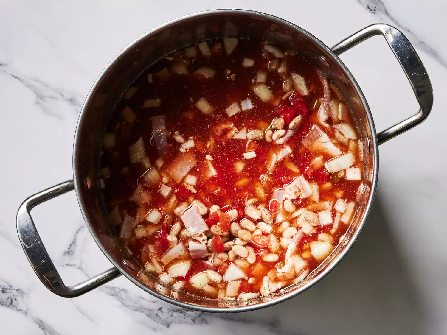 A pot of pinto beans in water, with tomatoes, bacon, onion, chili powder, cumin, and garlic powder.