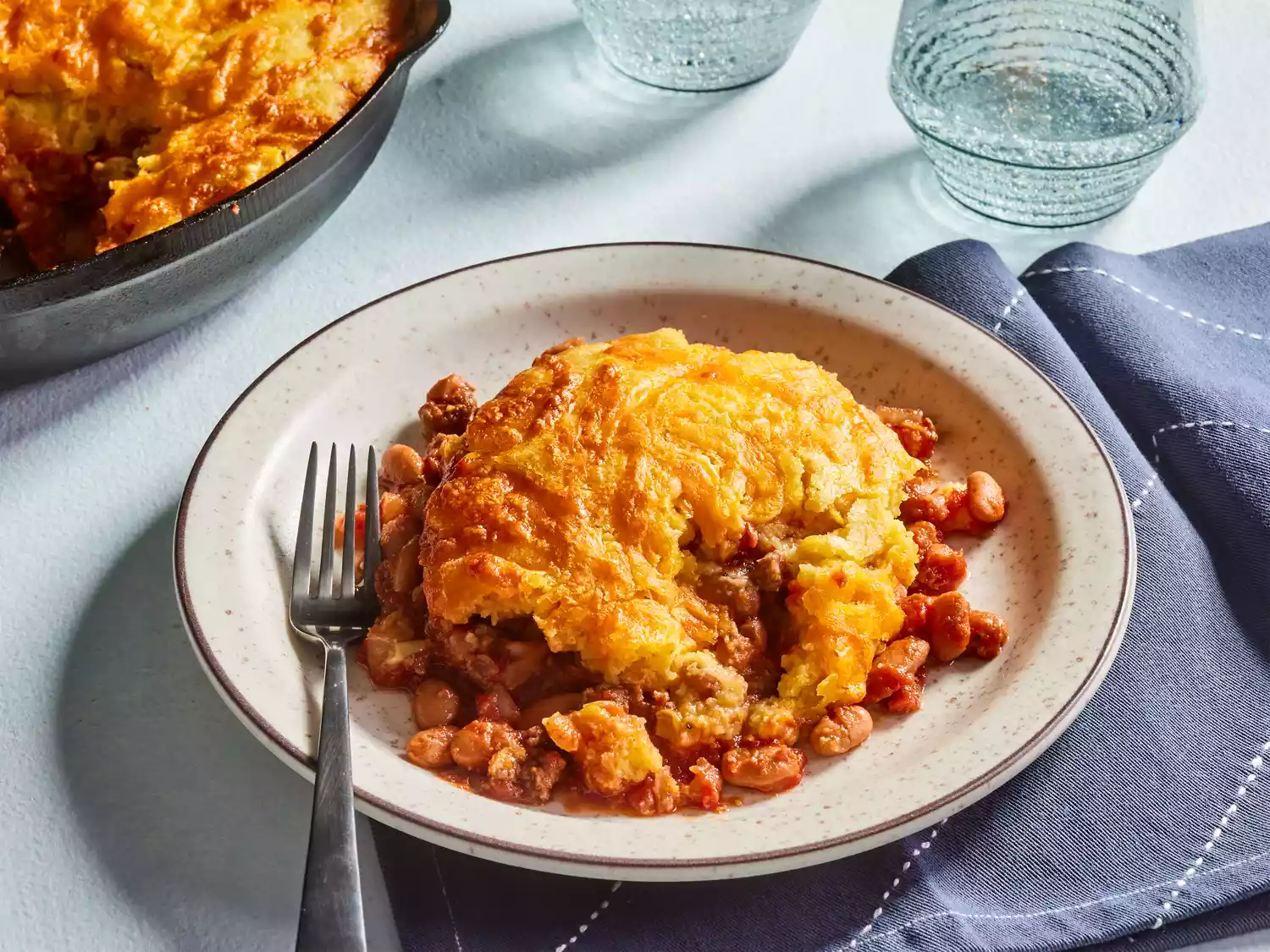 A serving of tamale casserole with a skillet of tamale casserole in the background