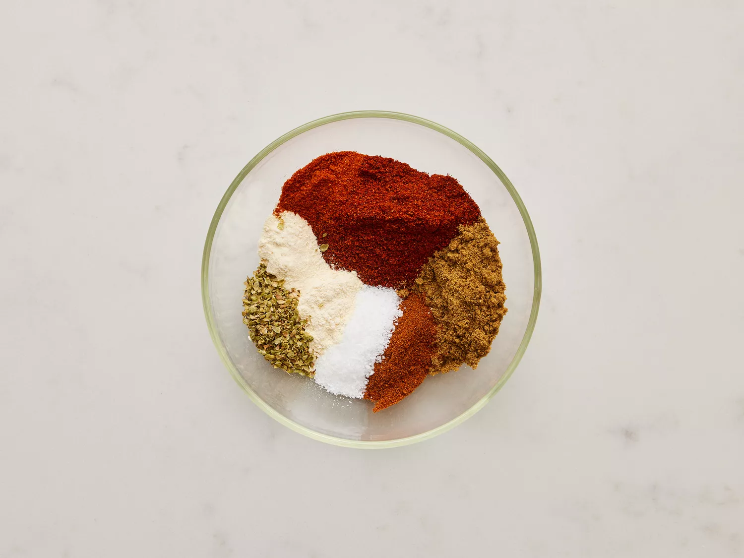 A small glass bowl with chili powder, cumin, paprika, salt, garlic powder, onion powder, oregano, and cayenne