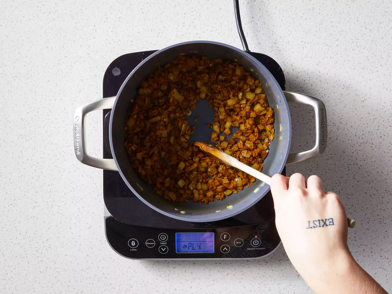 A wooden spoon stirring chopped onion together with garlic, coriander, turmeric, garam masala, red pepper flakes, curry powder, cumin, and salt