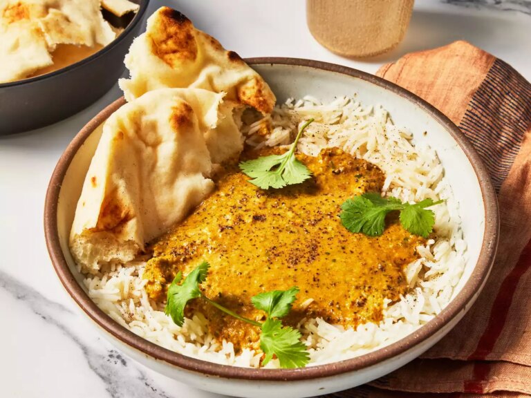 A bowl of rice covered in basic curry sauce, topped with cilantro and served with naan