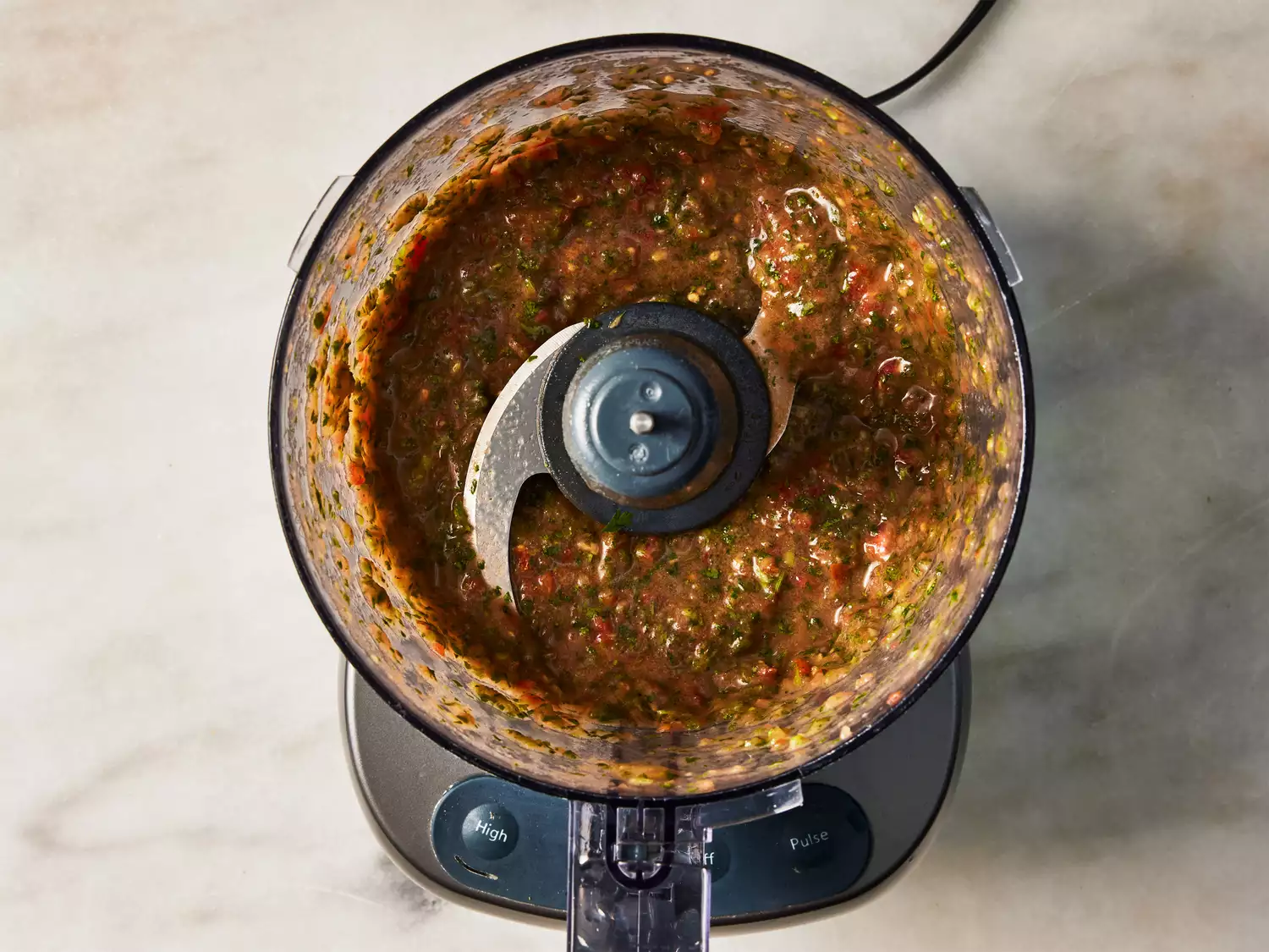A food processor with processed tomato, chile peppers, and cilantro