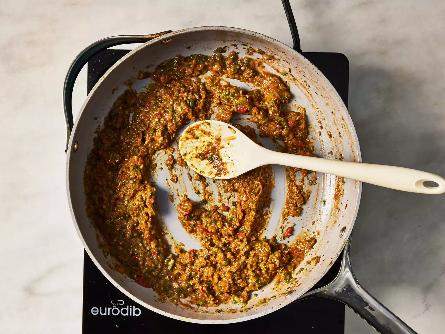 A pan with the pureed onion mixture and the pureed tomato mixture being stirred with a wooden spoon