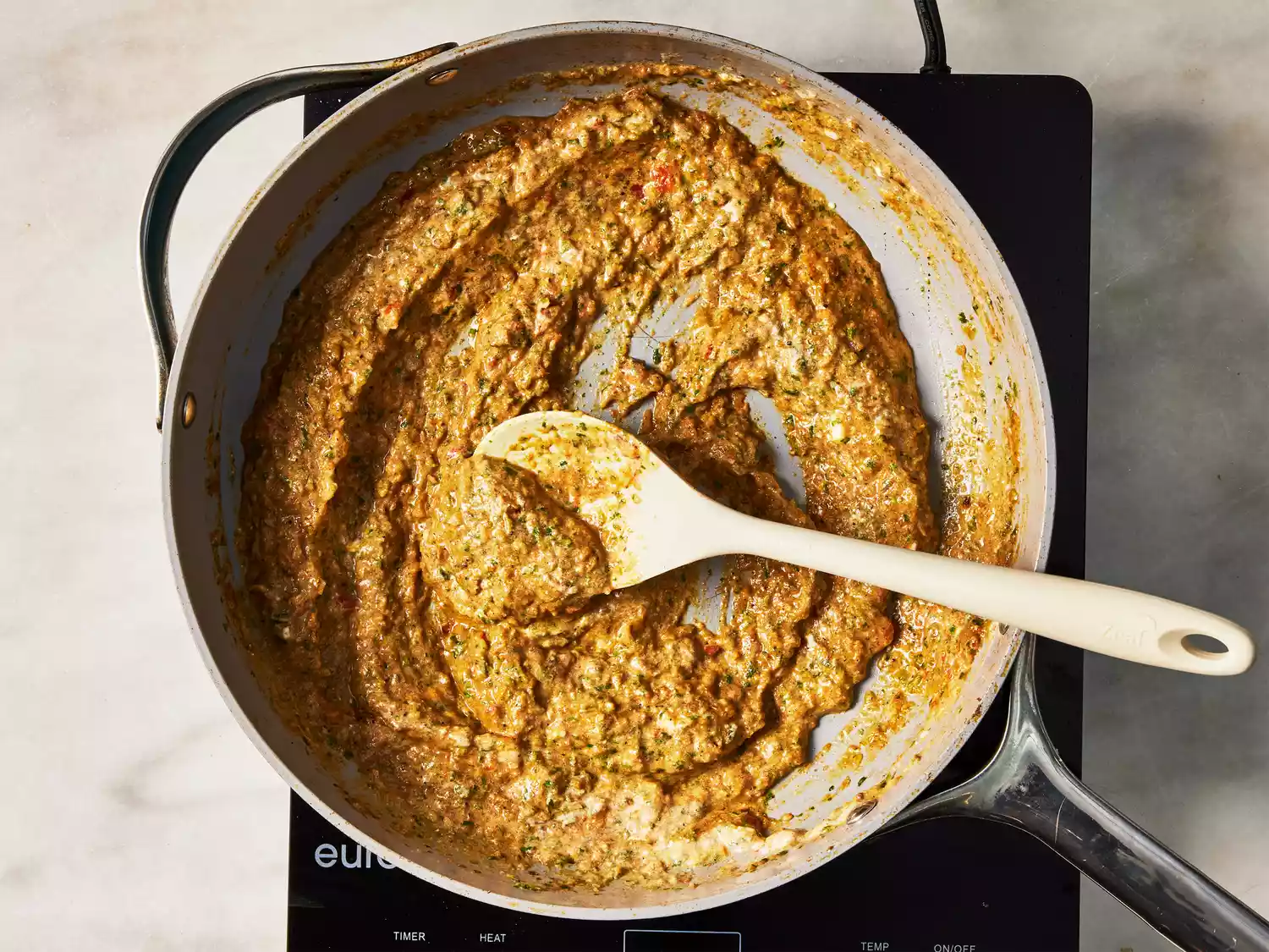 A pan of pureed seasoned onions and tomatoes being stirred with yogurt