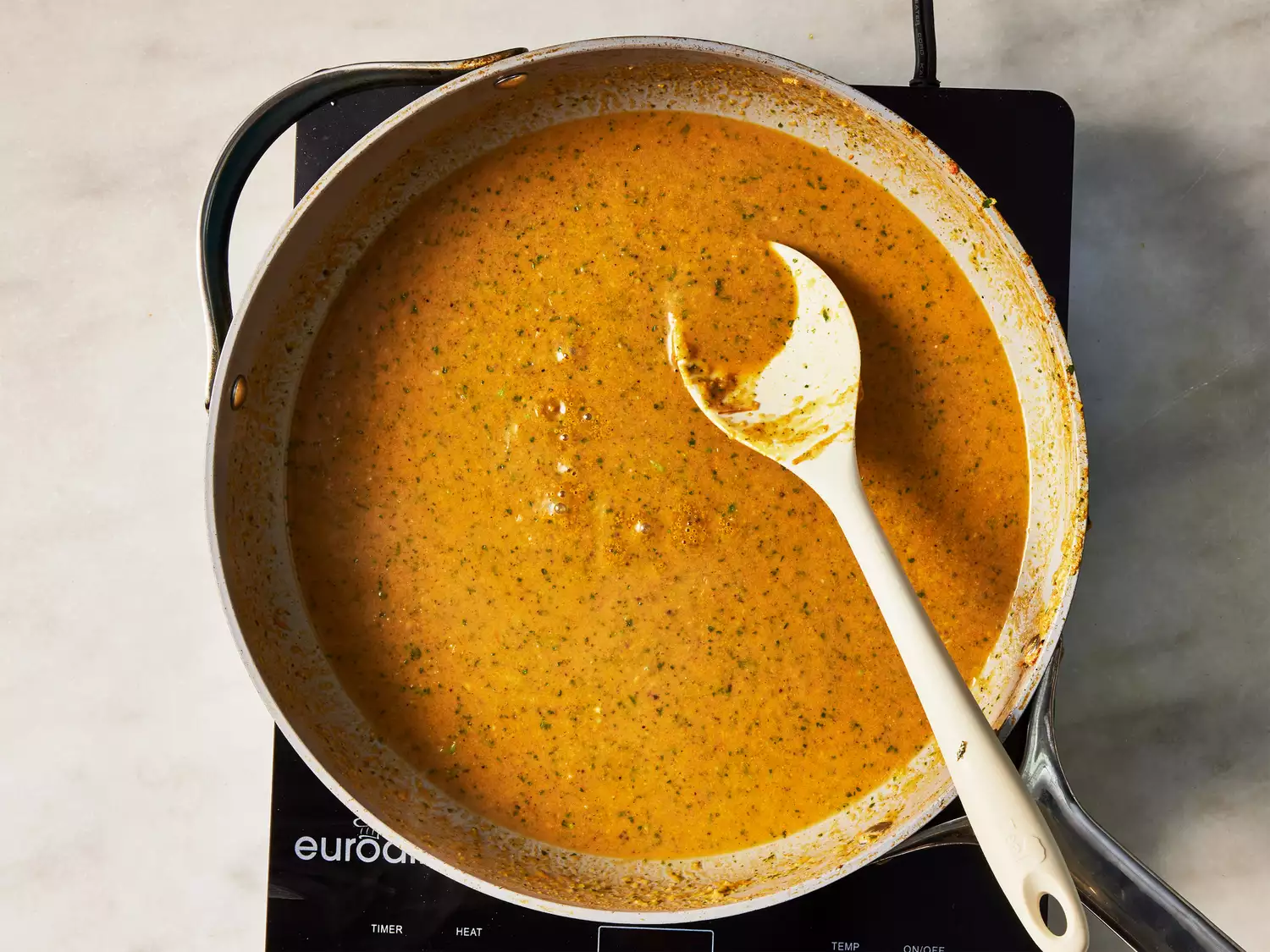 A pan of curry sauce being stirred with a wooden spoon