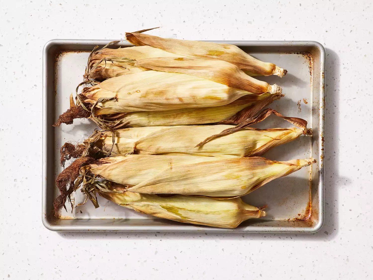 A baking sheet with roasted corn in husks