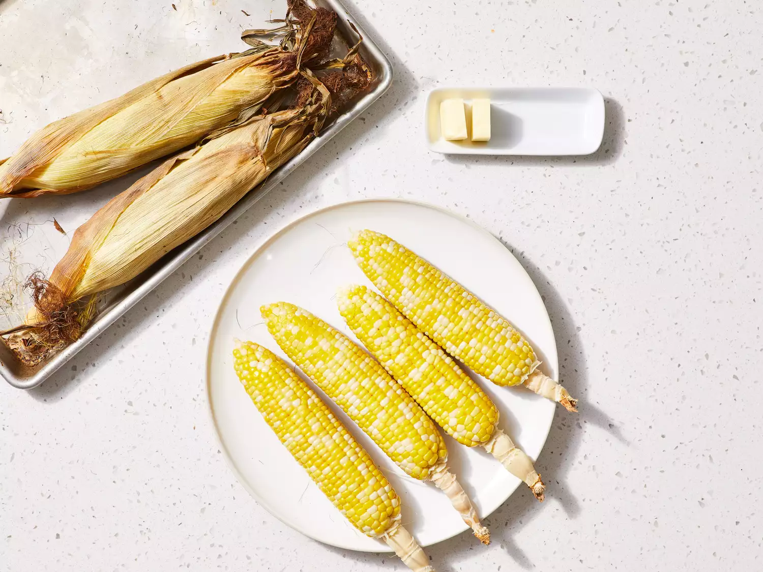 A plate with peeled ears of corn, topped with butter
