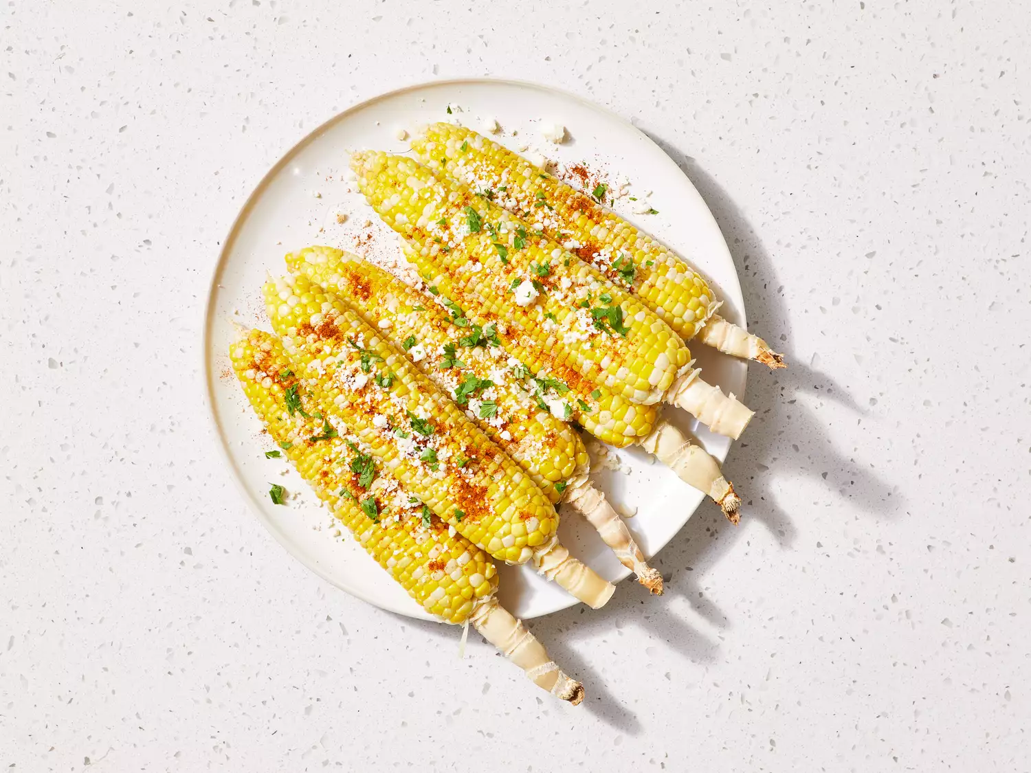 A platter of ears of corn topped with cotija cheese, cilantro, lime juice, and chili powder
