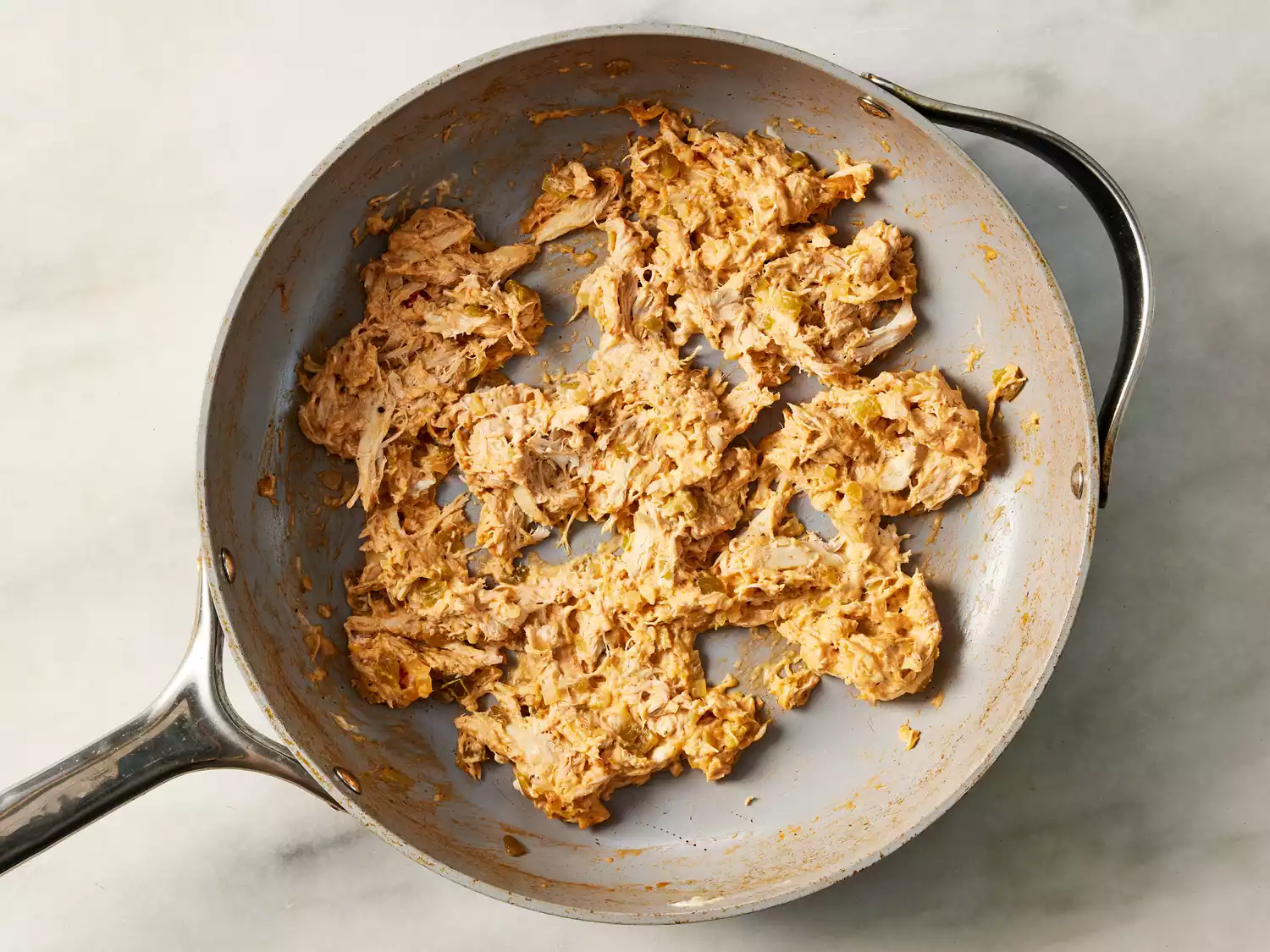 A pan with seasoned shredded chicken with Mexican tomato sauce and melted cheese