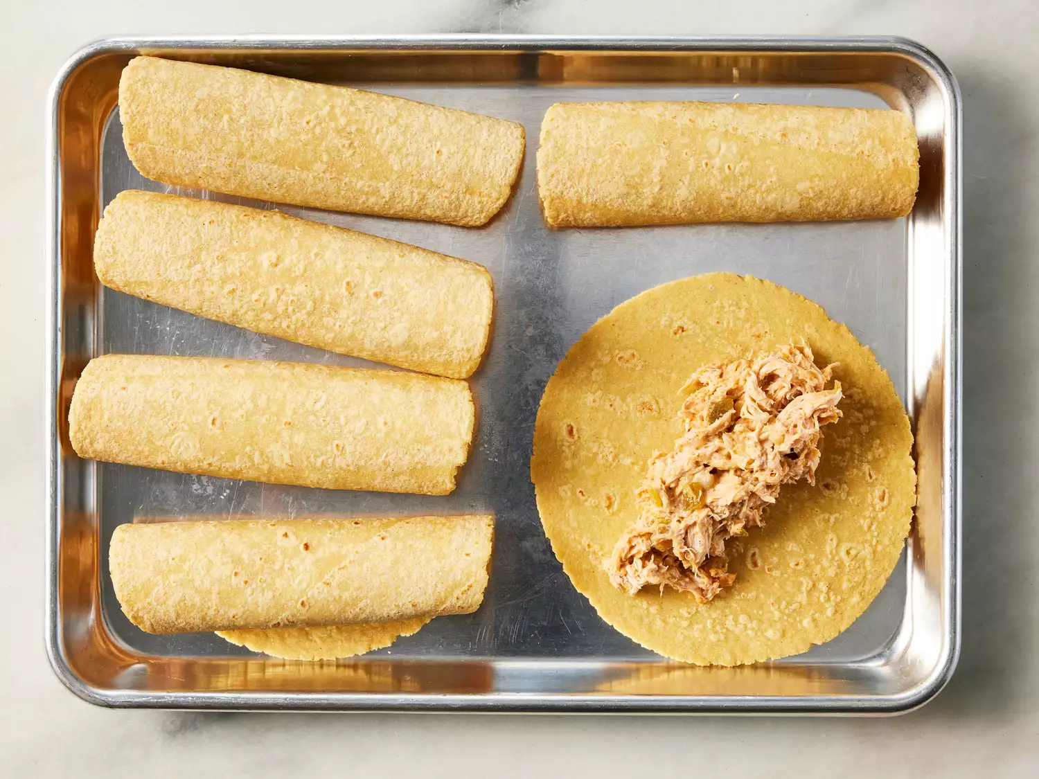 A baking sheet with warmed tortillas rolled around shredded chicken filling