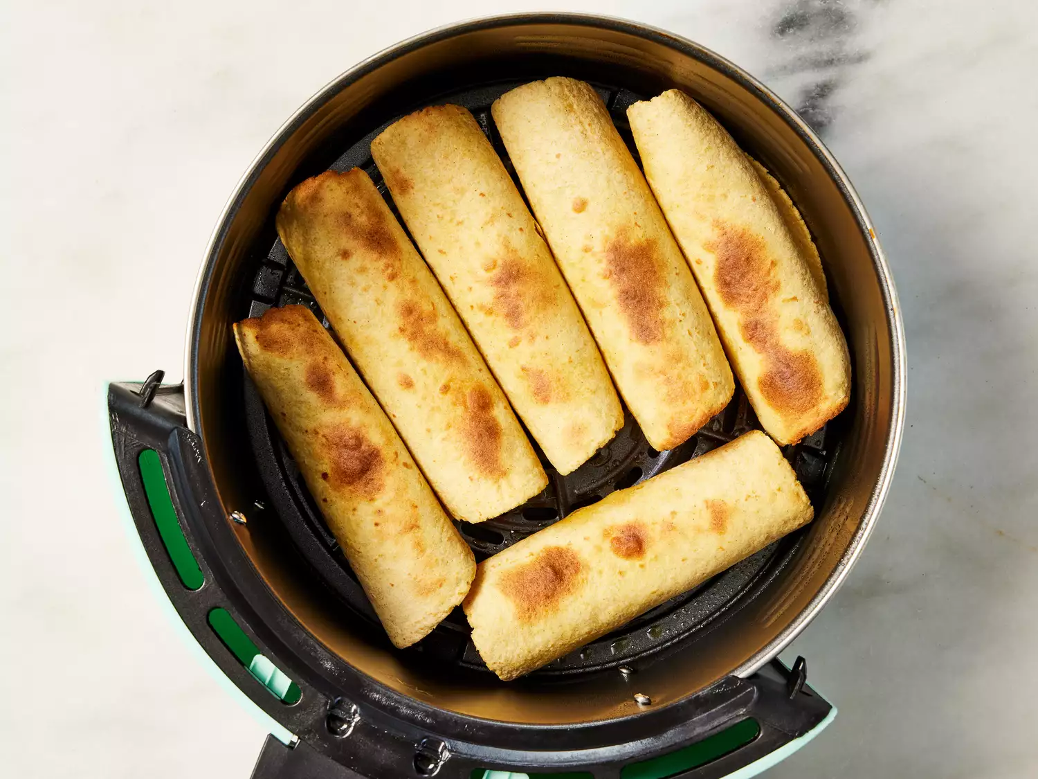 An air fryer basket with chicken taquitos
