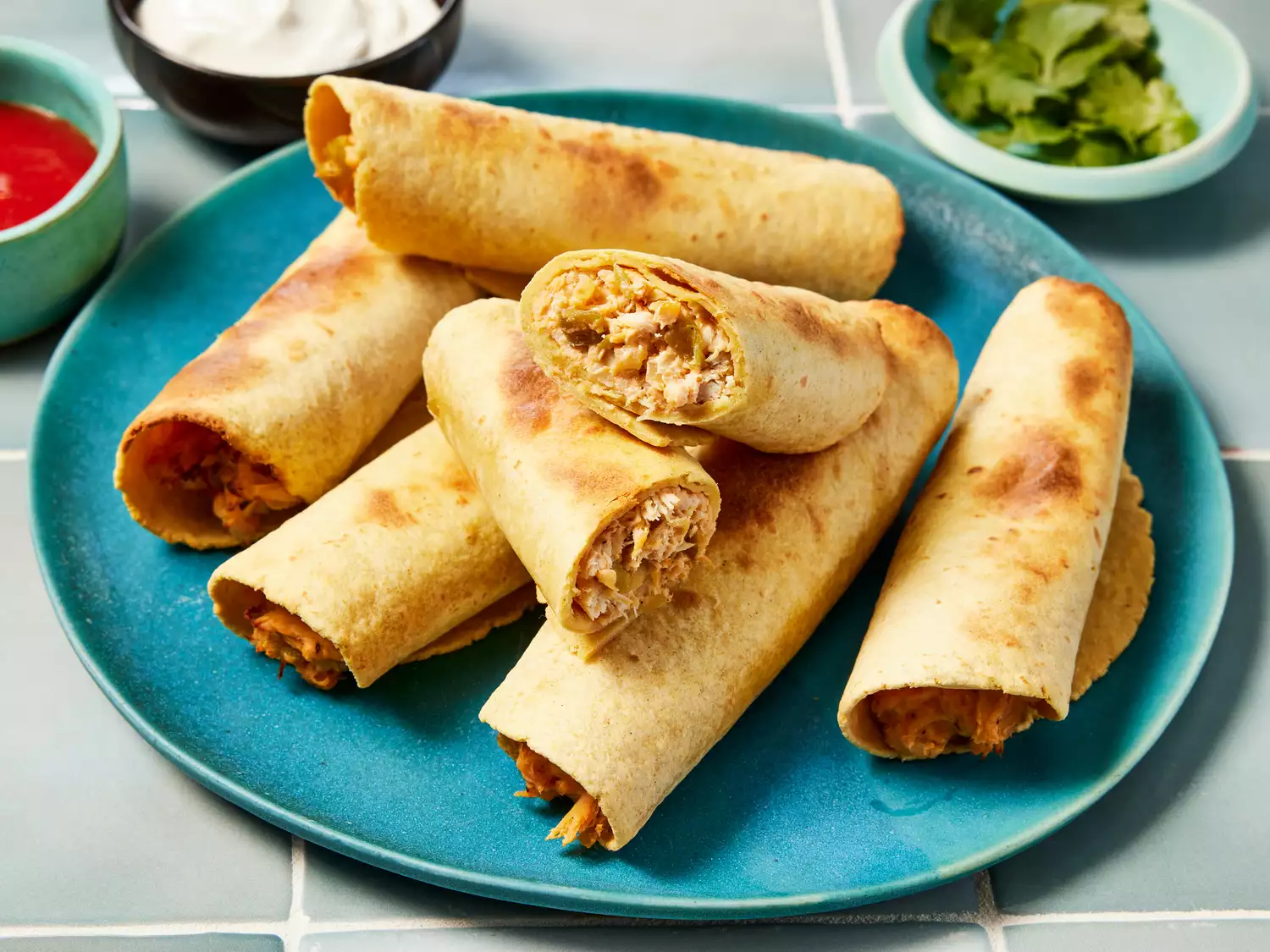 A plate of air fryer chicken taquitos served with salsa, sour cream, and cilantro