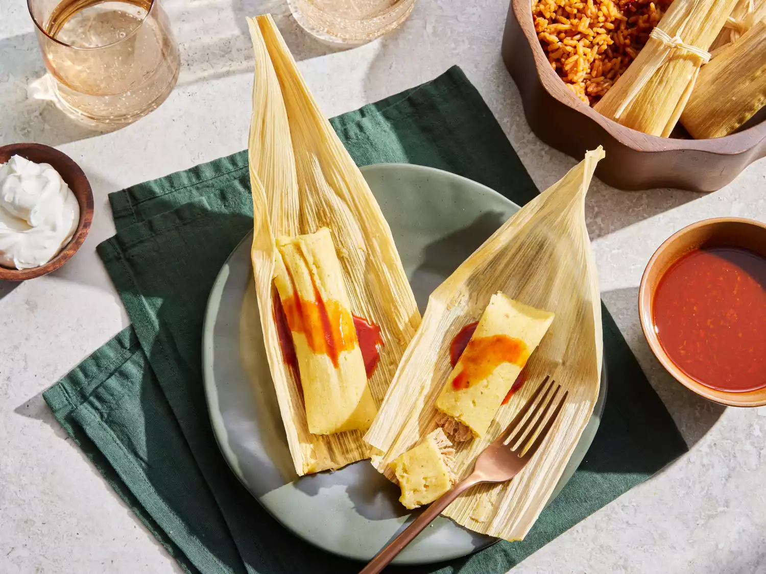 A plate with two tamales with the husks removed, topped with salsa and served with sour cream