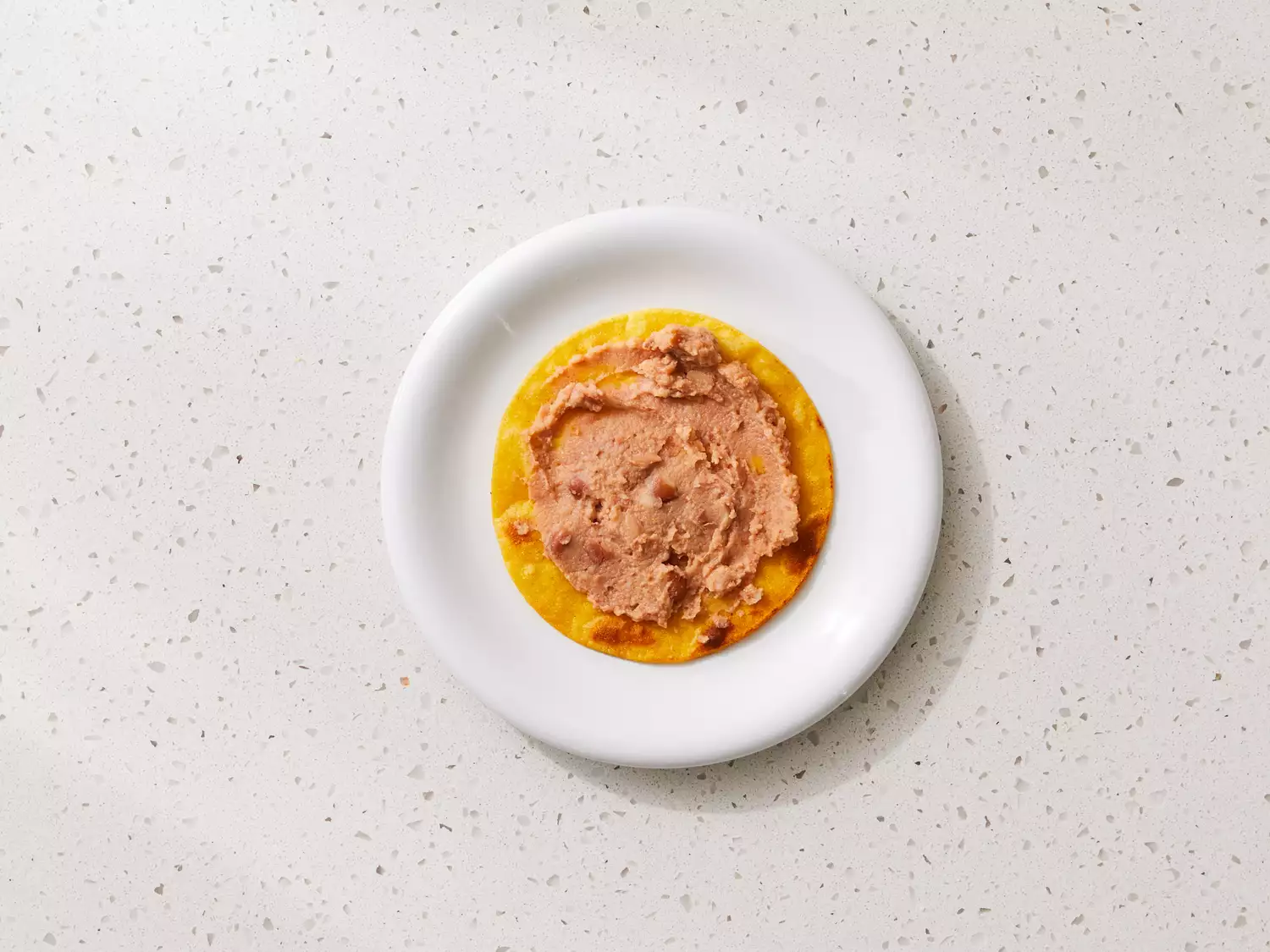 A plate with a browned tortilla topped with refried beans