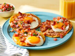 A plate of authentic huevos rancheros, topped with fresh salsa and crumbled bacon