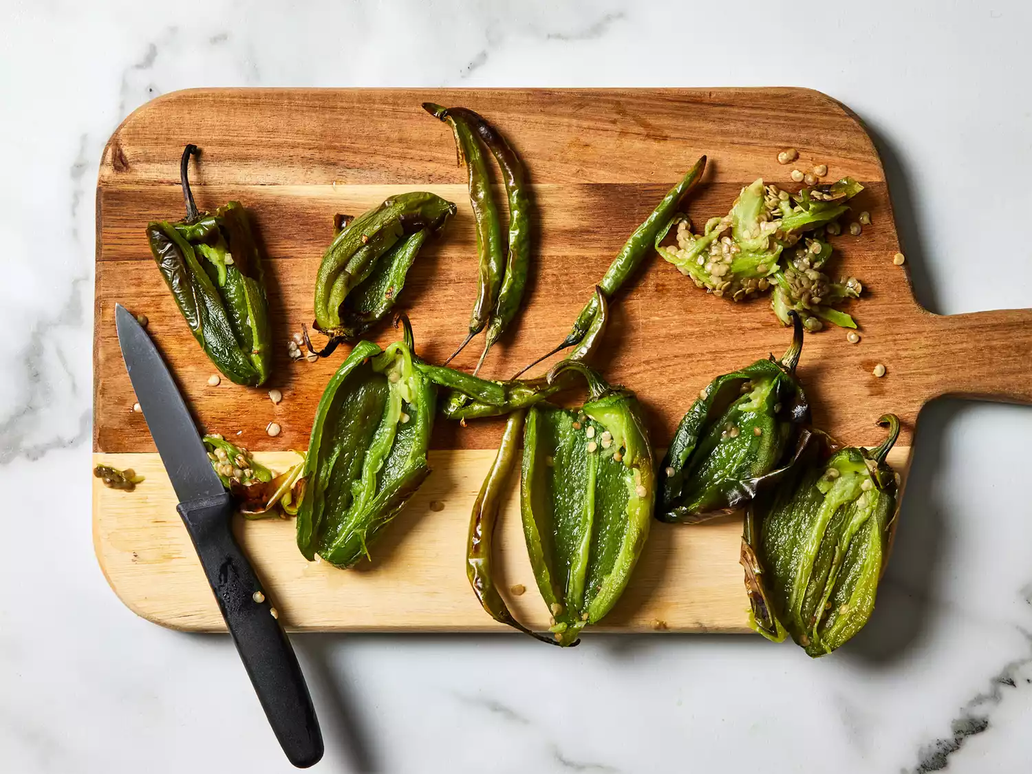 A cutting board with charred chile de arbols with seeds removed, and slit lengthwise