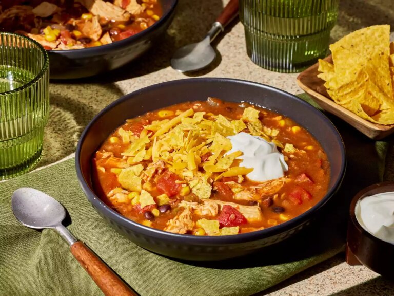 A bowl of slow cooker chicken taco soup, topped with crushed tortilla chips and sour cream