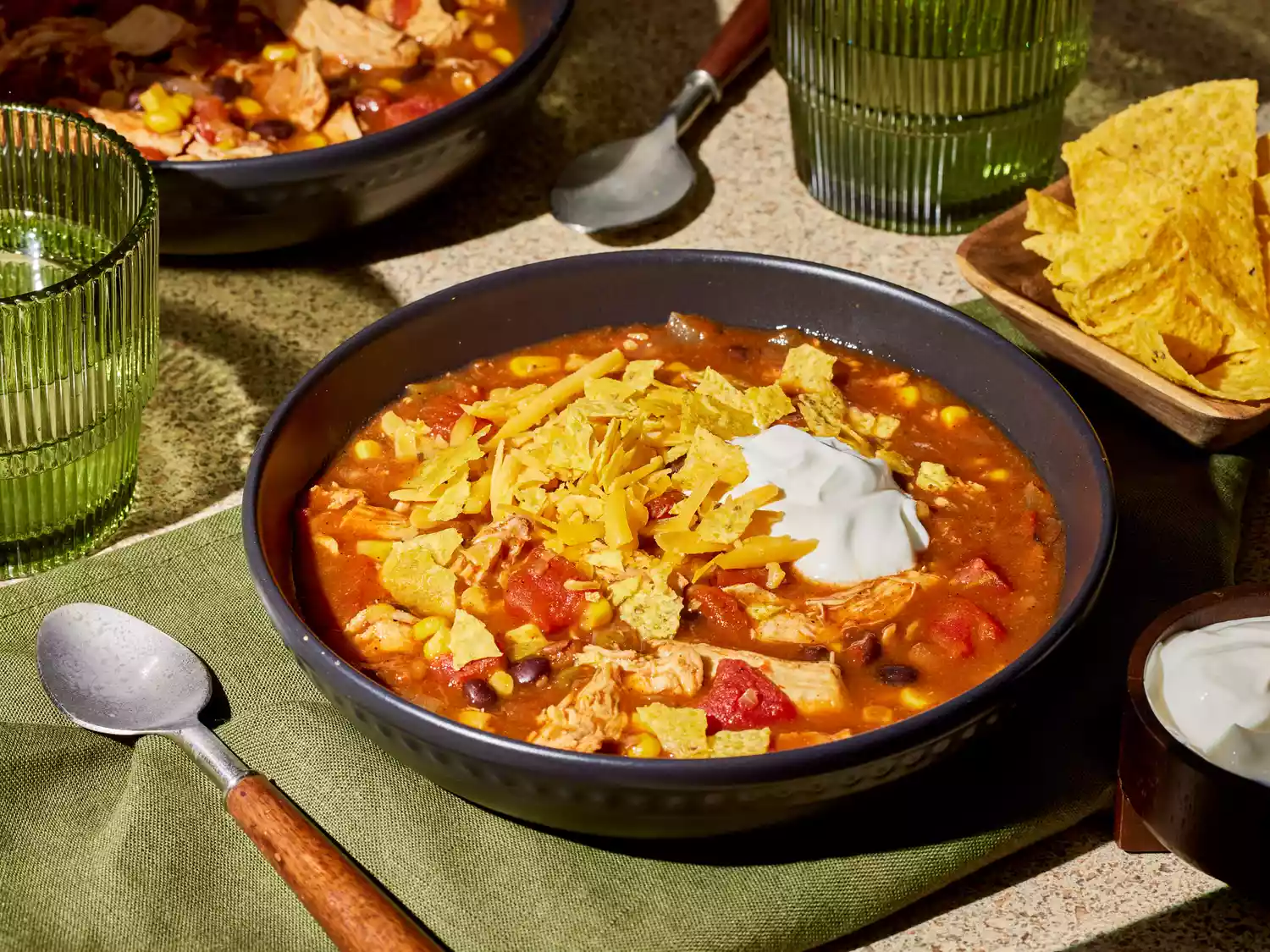 A bowl of slow cooker chicken taco soup, topped with crushed tortilla chips and sour cream