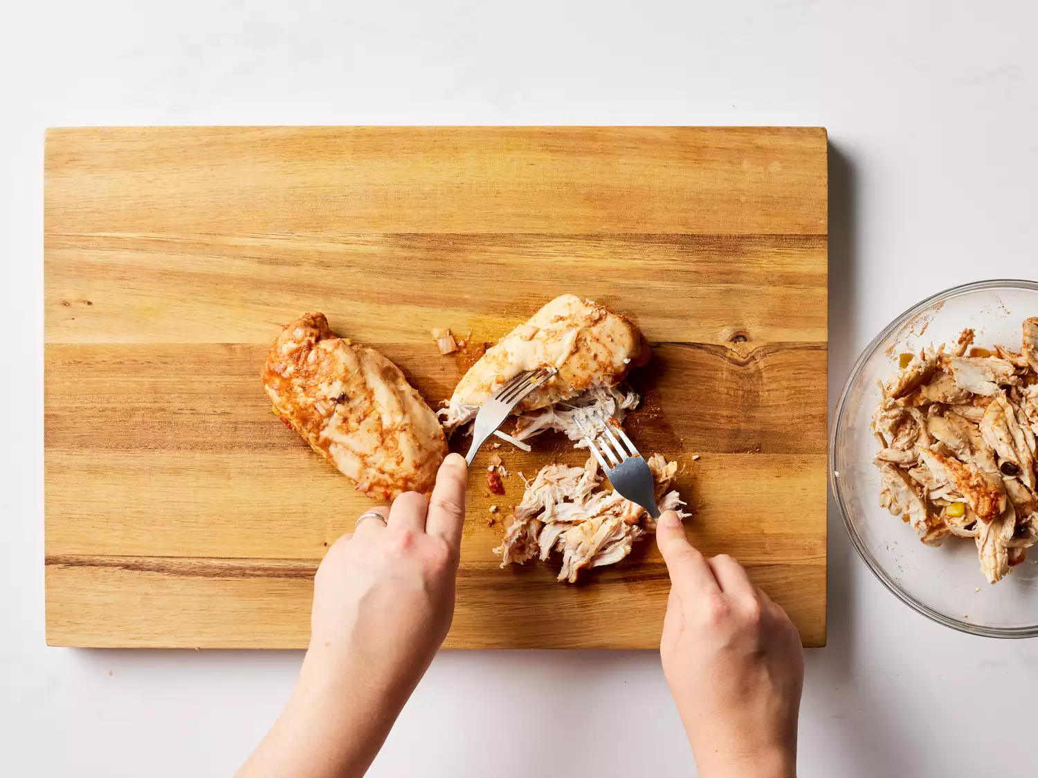 A cutting board with chicken breasts being shredded with two forks