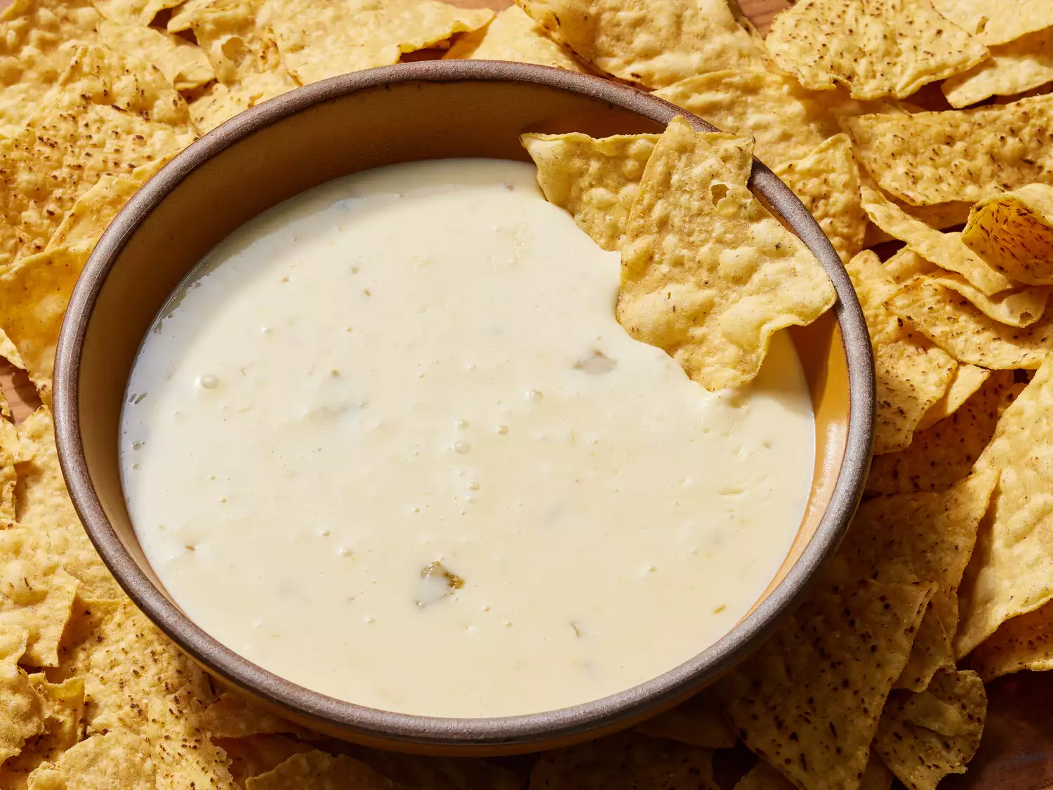 A bowl of mexican white queso dip, surrounded by tortilla chips