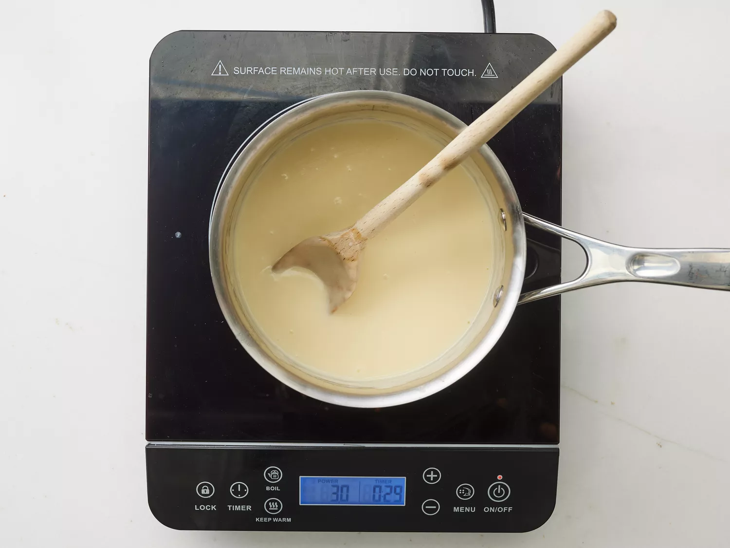 A saucepan with melted butter, cheese, and milk with a wooden spoon