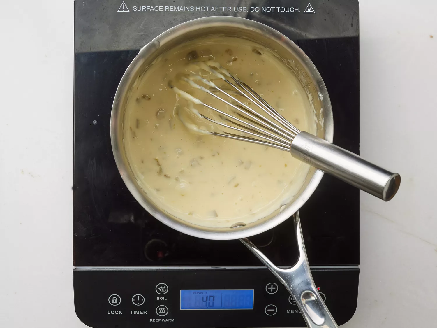 A whisk mixing in green chilies, cumin, garlic powder, onion powder, and cayenne pepper in a small saucepan with cheese sauce