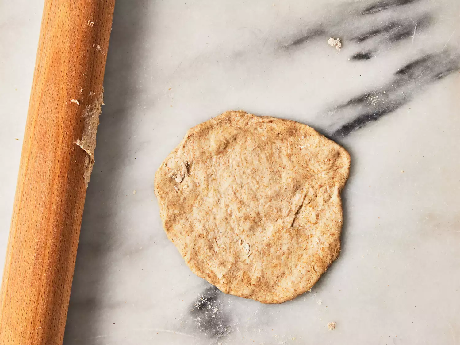 A rolled out piece of dough on a marble surface with a rolling pin