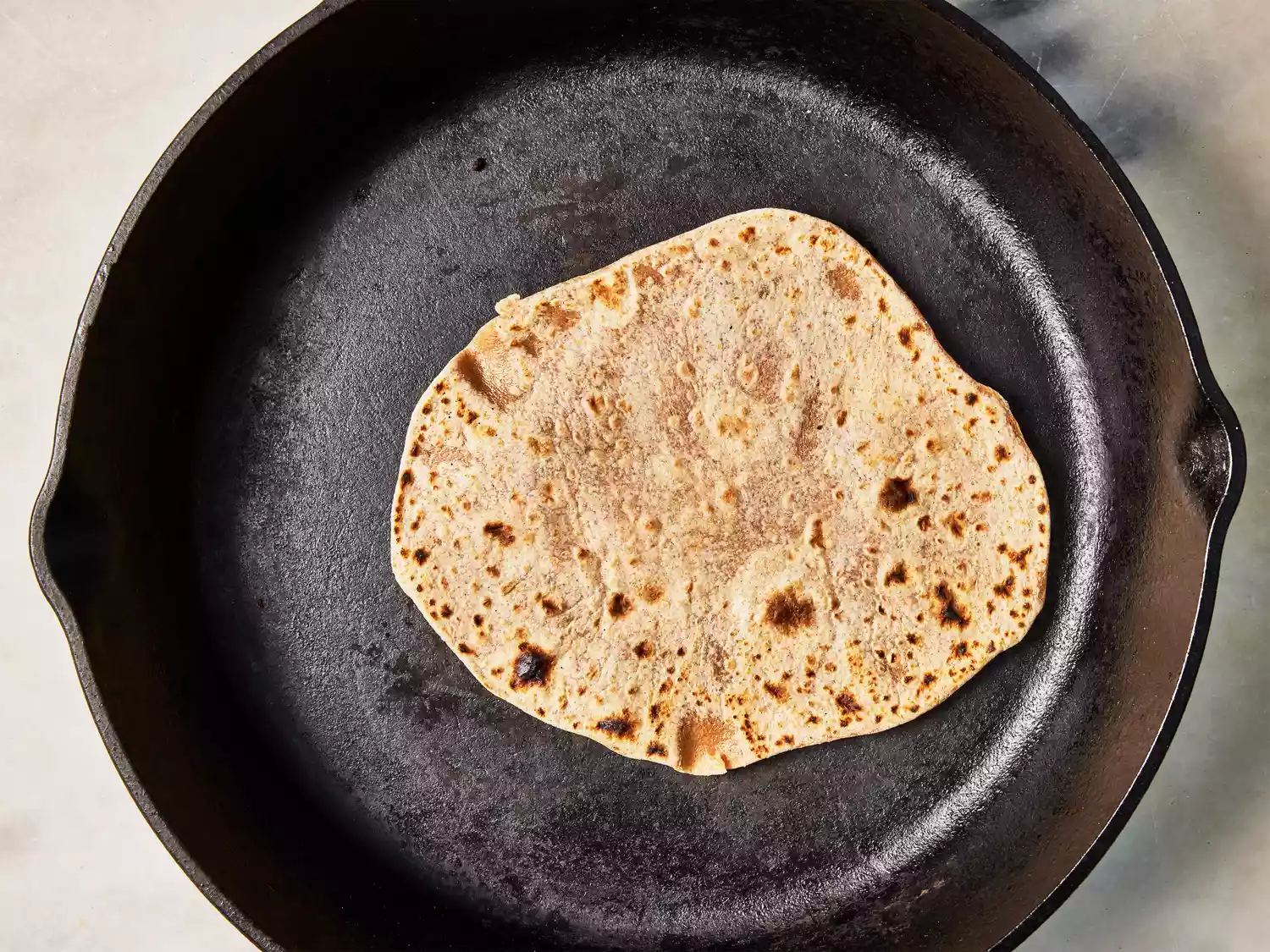 A cast iron skillet with a browned chapati 