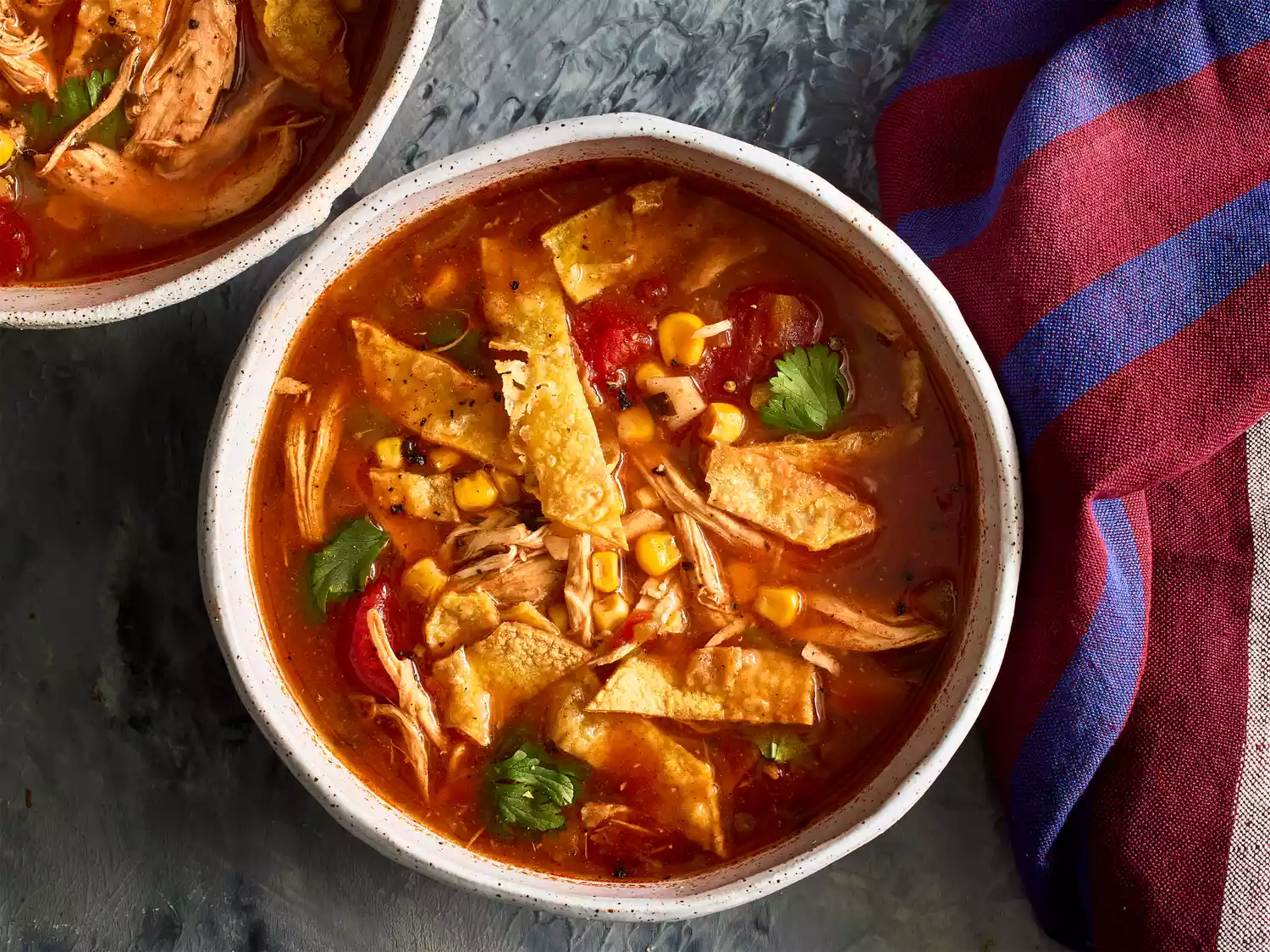 Slow cooker chicken tortilla soup, garnished with crunchy tortilla strips and cilantro