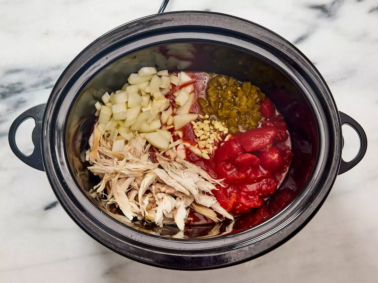 A slow cooker with shredded chicken, tomatoes, enchilada sauce, green chiles, onion, and garlic