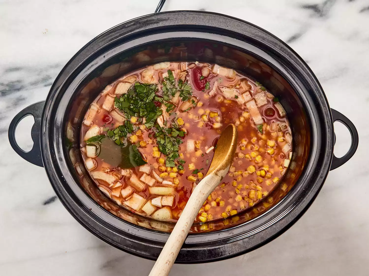 A spoon stirring a slow cooker with chicken soup