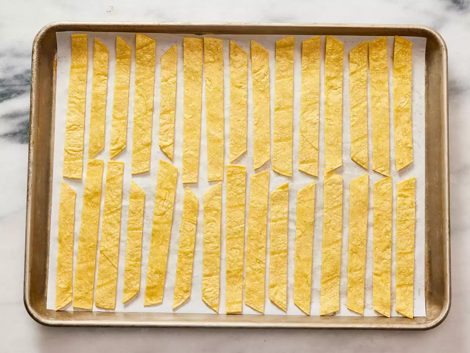 A parchment lined-baking sheet with striped of oiled tortillas