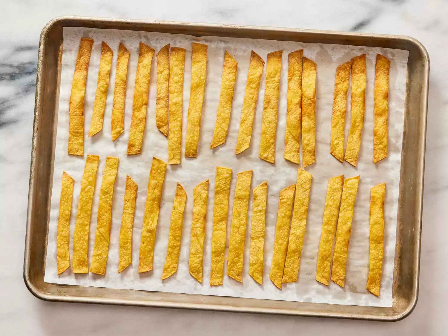 A parchment paper-lined baking sheet of crunchy tortilla strips