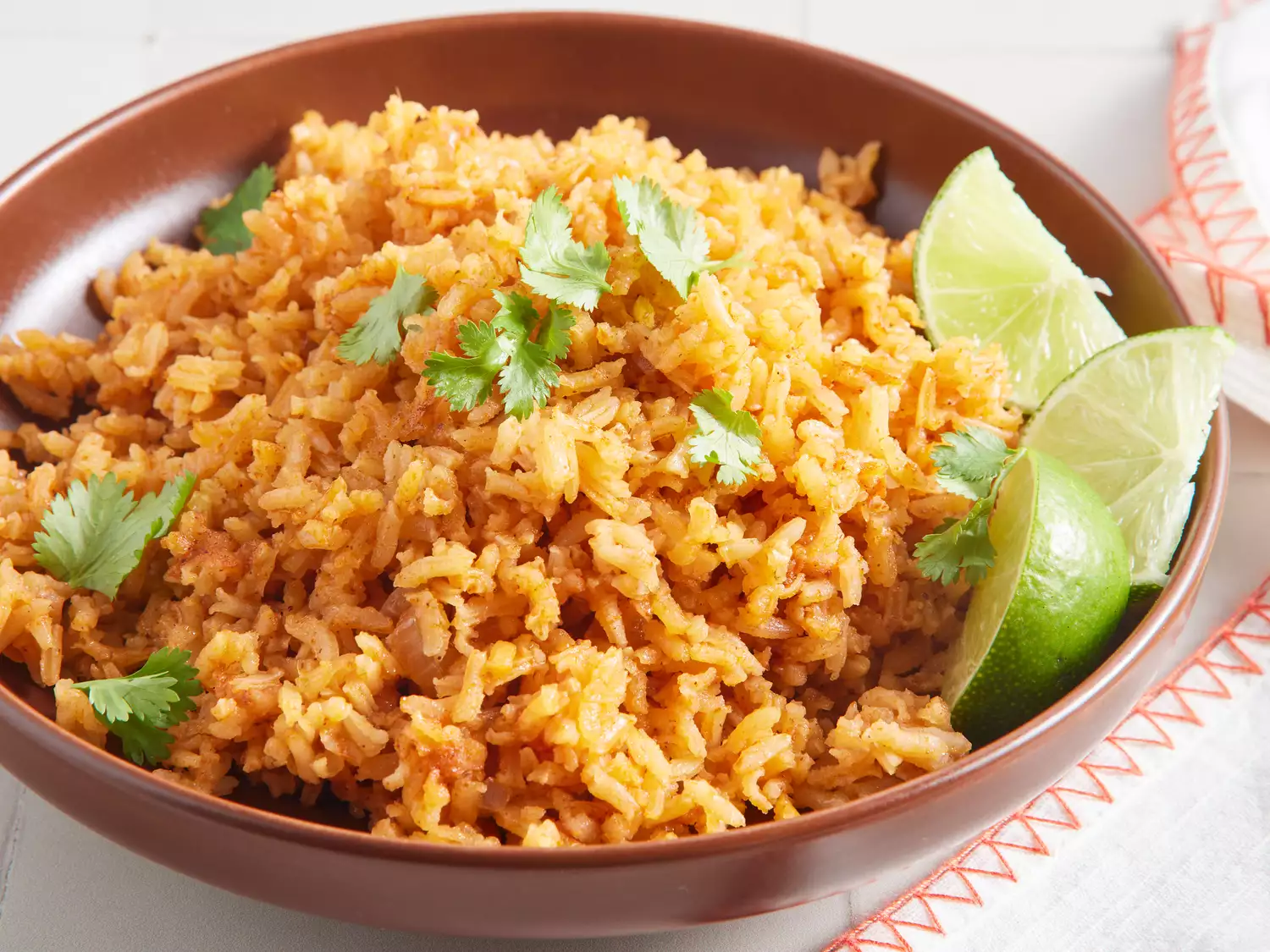 A bowl of mexican rice topped with fresh cilantro and served with lime wedges