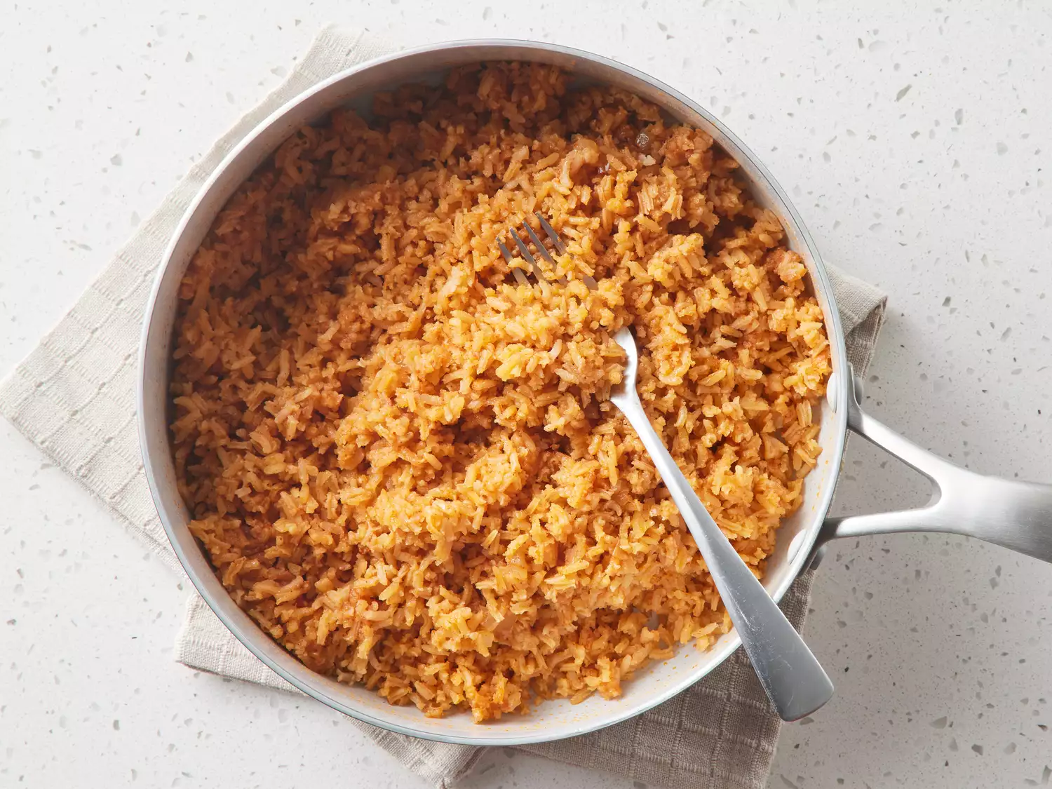 A pan of cooked Mexican rice, fluffed with a fork