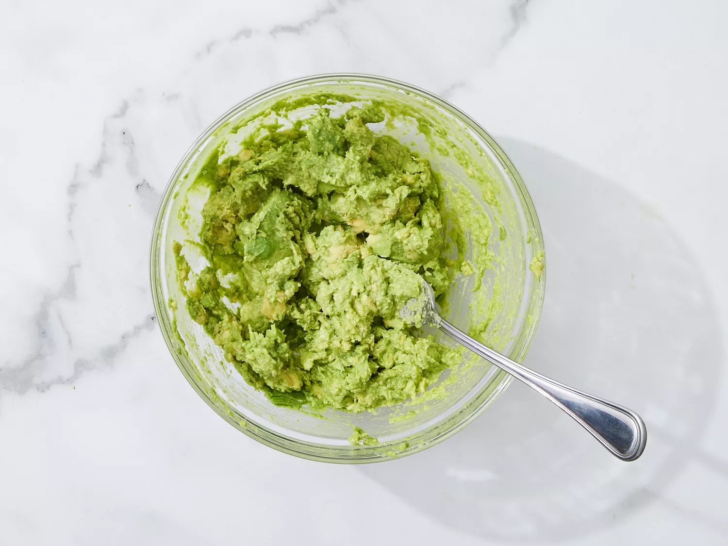 A glass bowl with mashed avocados and a fork