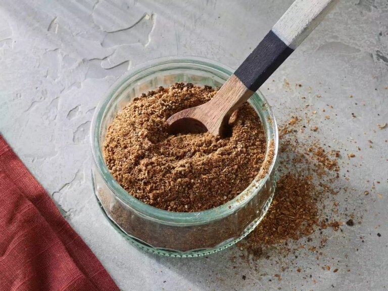 A small glass jar of homemade garam masala spice mix with a wooden spoon