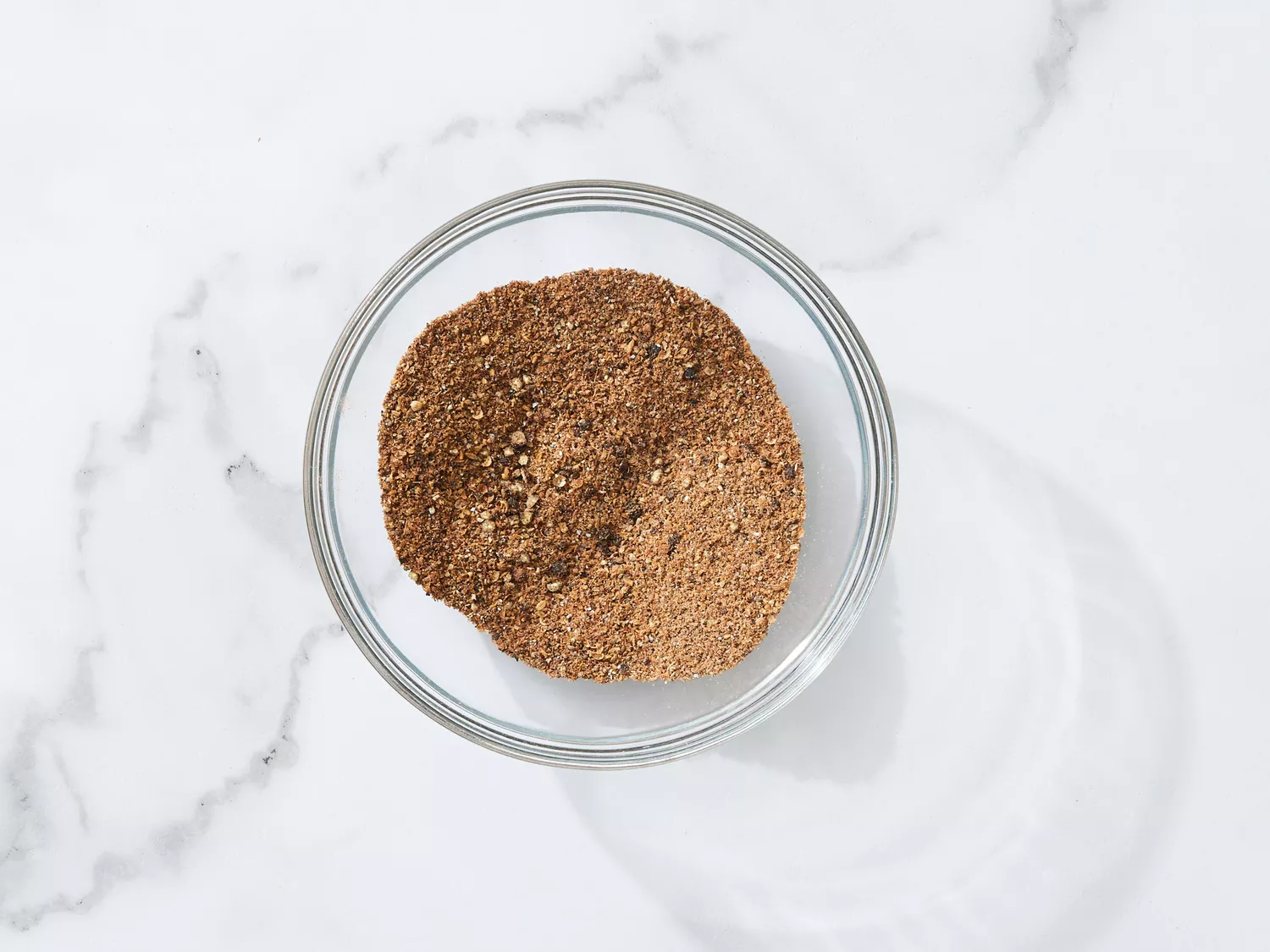 A glass bowl with cumin, coriander, cardamom, pepper, cinnamon, cloves, and nutmeg mixed together