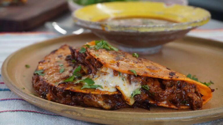Birria de res tacos (beef birria tacos) close up with dipping sauce, topped with cilantro