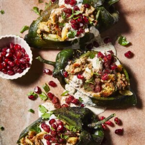 Close up on three chiles en nogada on a board with a side of pomegranates