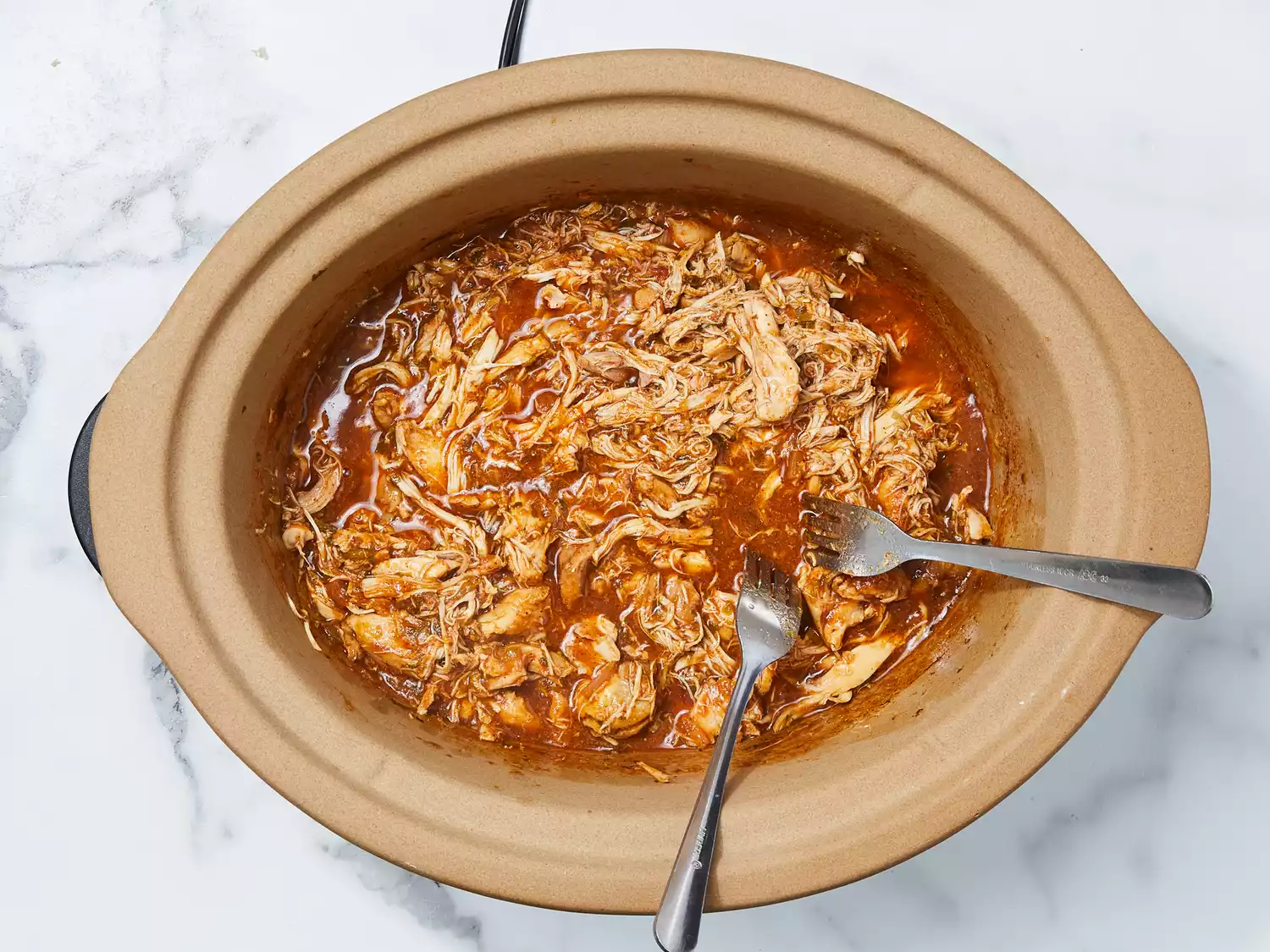 cooked chicken shredded with two forks in the slow cooker.