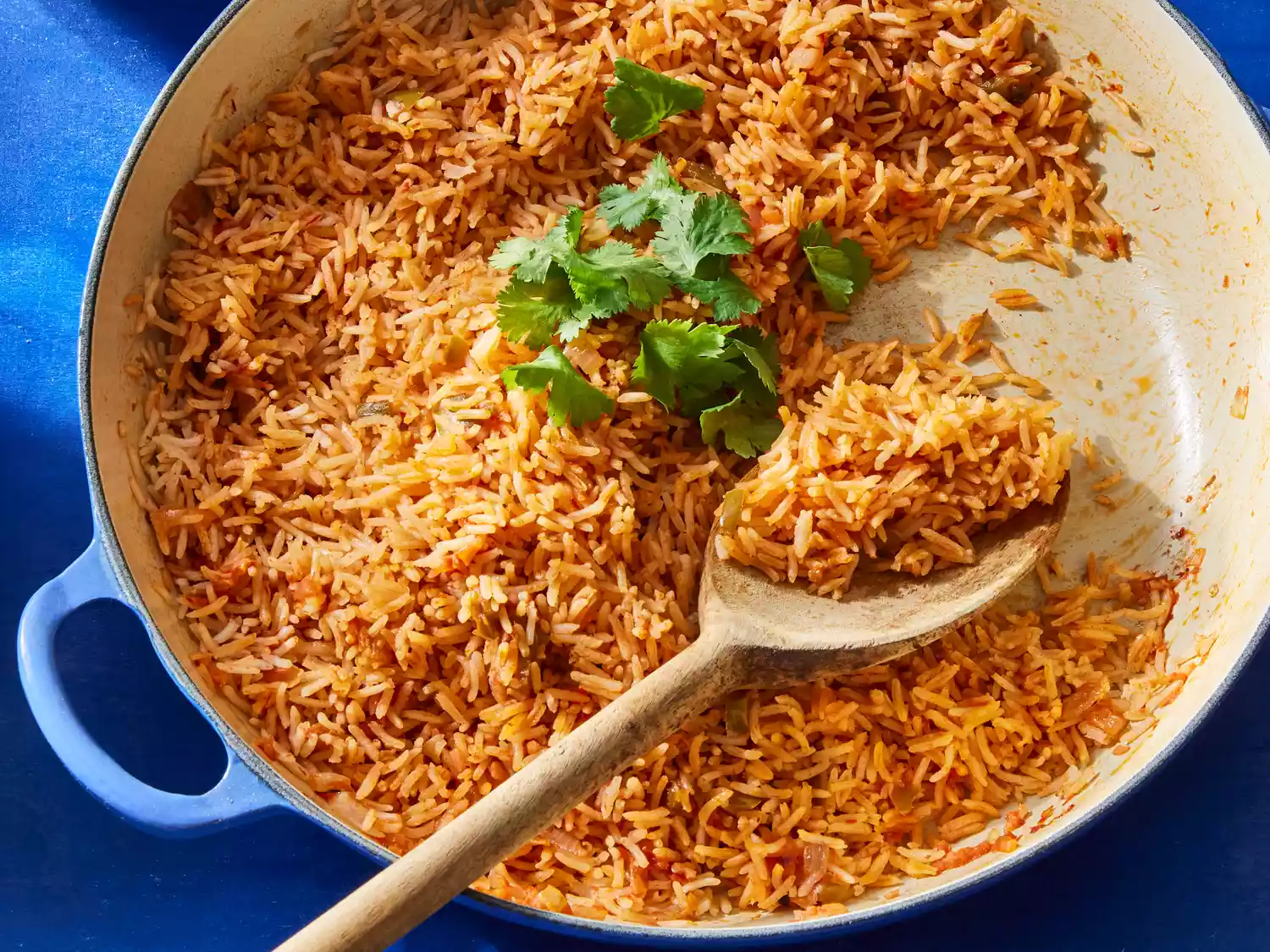 A large pot of spanish rice with a wooden spoon, topped with fresh cilantro leaves