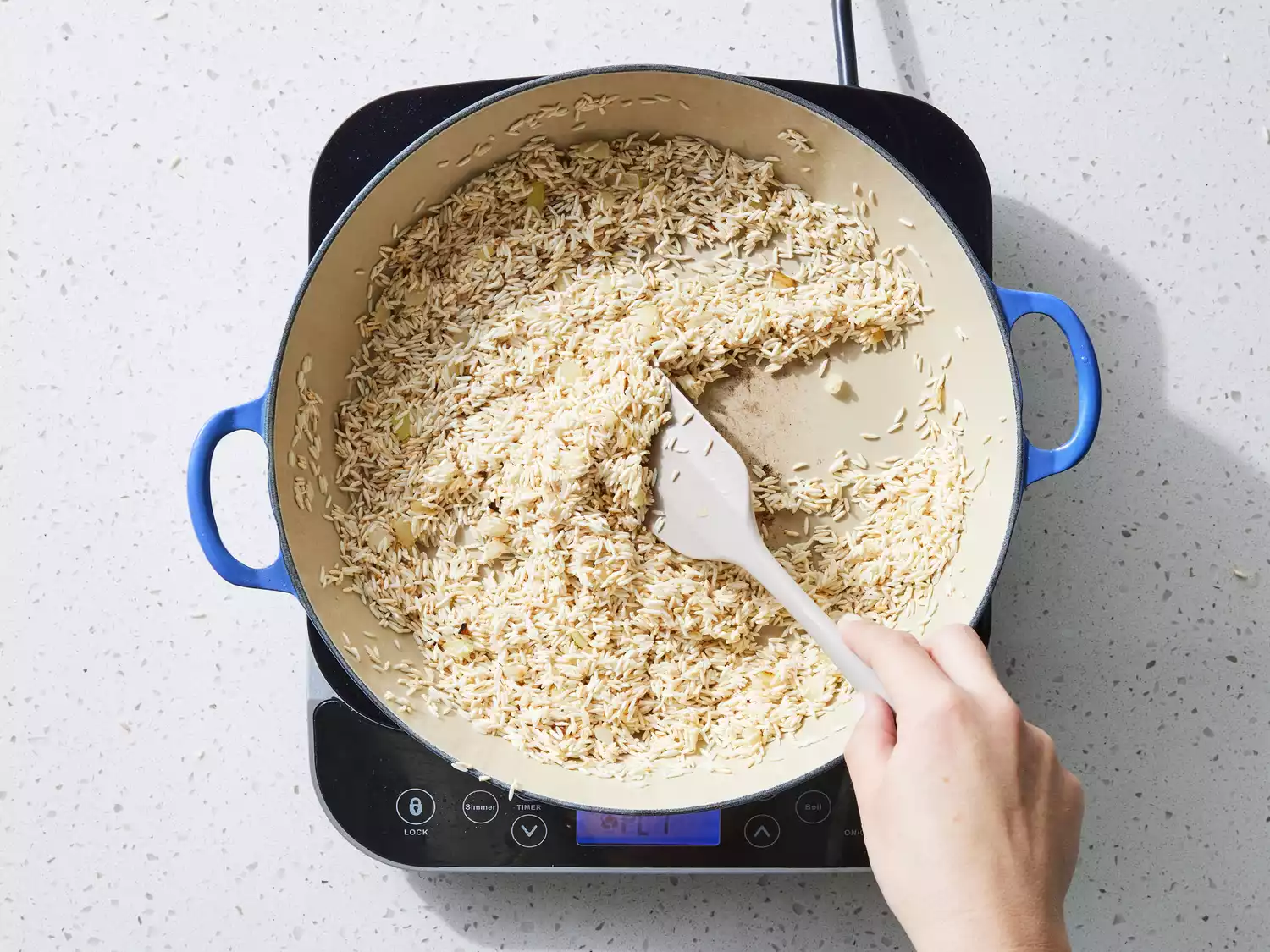 A spatula stirring rice in a large pot with oil and chopped onions