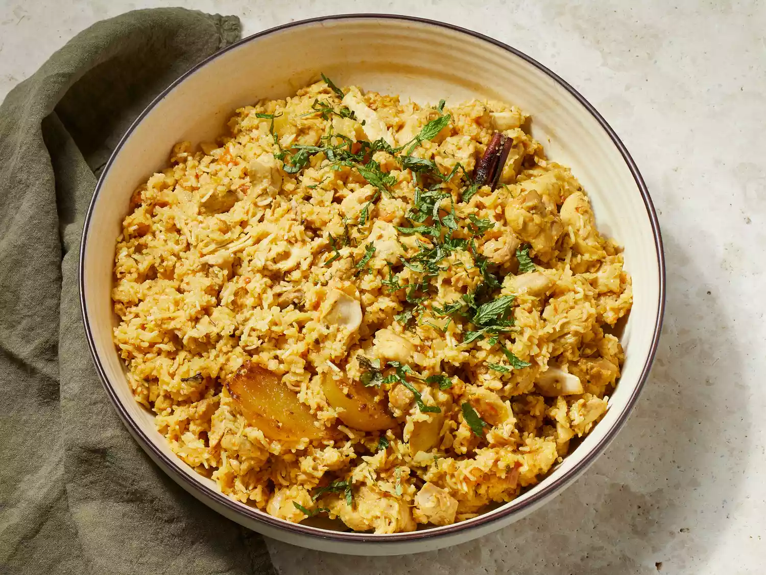 Close up on a bowl of chicken biryani, garnished with chopped mint leaves.